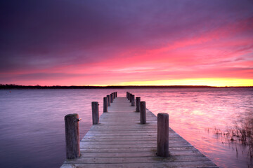 Obraz premium purple sunset light over a long wooden rustic pier at the lake