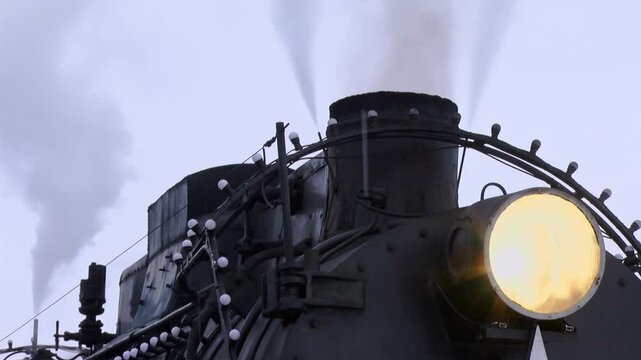 The vintage steam locomotive evokes a strong sense of nostalgia with its powerful billowing steam and bright headlights