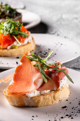 Close-up of two bruschettas topped with cream cheese, smoked salmon, and arugula on a white plate, garnished with herbs. Perfect for culinary, food photography, and gourmet cuisine themes.