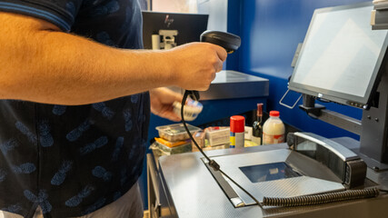 A Caucasian person using a barcode scanner at a self-checkout counter symbolizes modern retail convenience and technology integration