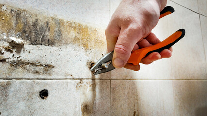 A person uses pliers to repair a damaged tiled wall, addressing home maintenance and renovation challenges