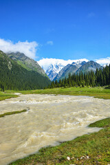 Idyllic summer landscape with hiking trail in the mountains with beautiful fresh green mountain pastures, river with reflection and forest.