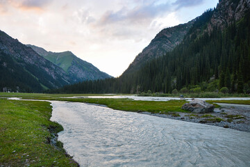 Idyllic summer landscape with hiking trail in the mountains with beautiful fresh green mountain pastures, river with reflection and forest.