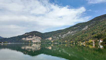 Fototapeta premium Serene landscape of a tranquil lake reflecting lush green hills under a cloudy sky, perfect for relaxation and nature escapes