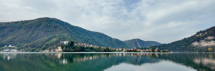 Fototapeta premium Picturesque lakeside village surrounded by lush green mountains reflects on calm water, ideal for exploring tranquility and nature tourism