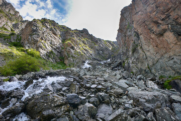 Idyllic summer landscape with hiking trail in the mountains with black stones, green mountain pastures and rocks.