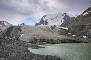 Idyllic winter landscape with hiking trail in the mountains. Rocks, snow, lake, glacier and stones.