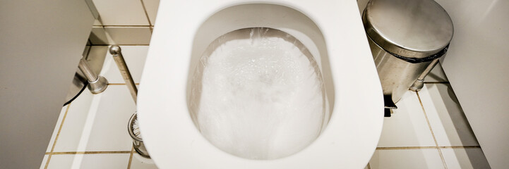 A toilet flushes clean water in a public restroom, highlighting sanitation and hygiene concerns
