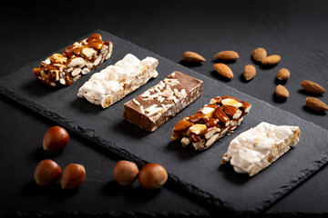 Assortment of gourmet nougat and nut bars on a sleek black slate plate in a serene and elegant setting evoking sopihstication.