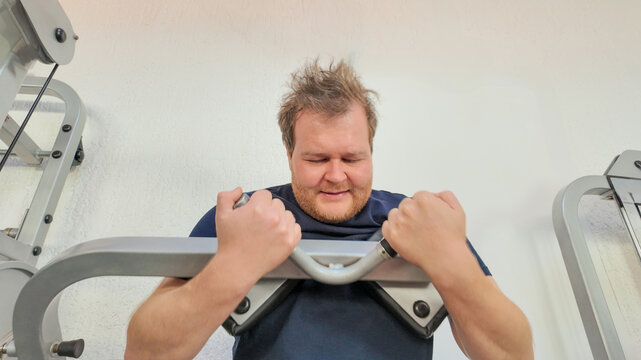 A Caucasian man struggles with exercise on a gym machine, highlighting fitness challenges and perseverance in weight loss goals