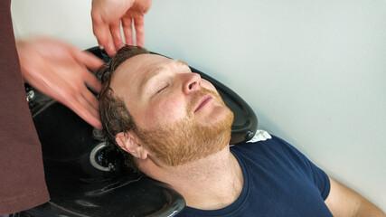 Obraz premium Man receiving a relaxing shampoo at a salon, highlighting self-care and grooming services, concept of relaxation and wellness