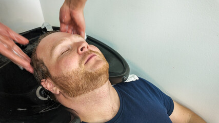 Fototapeta premium A Caucasian man enjoys a relaxing hair wash at a salon, highlighting self-care and grooming concepts