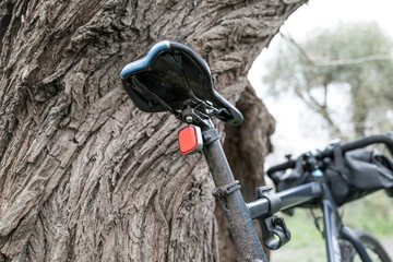 Rear view of a new but muddy cross bike showing the saddle and rechargeable rear LED light. Seen leaning against a forest tree after a cycle ride in the new forest, UK.