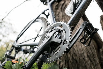 Obraz premium Low down view of a new but dirty cross bicycle showing the front cog and chain system. Seen leaning against a forest tree in rural UK.