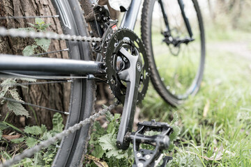 Fototapeta premium Low down view of a new but dirty cross bicycle showing the front cog and chain system. Seen leaning against a forest tree in rural UK.