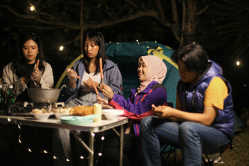 Friends Enjoying Outdoor Cooking at Night Around Campsite