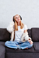 Fototapeta premium A woman relaxes on the sofa, enjoying music through her headphones. An attractive young girl takes advantage of her leisure time for rest and enjoyable activities at home.