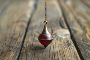 Red and bronze pendulum is hanging over a wooden background, swaying back and forth