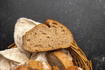 A rustic loaf of bread is placed on a wooden cutting board accompanied by a small bowl of flour, set against a dark textured background with a fabric piece to the side.