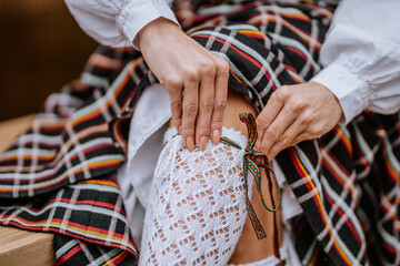 Close-up of hands adjusting a white lace stocking with a colorful ribbon over a traditional Latvian...