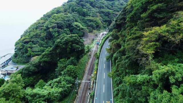 Captured on a cloudy day, this scenic view highlights the local train tracks running through mountain countryside, with surrounding fields and traditional houses adding charm to the tranquil atmospher
