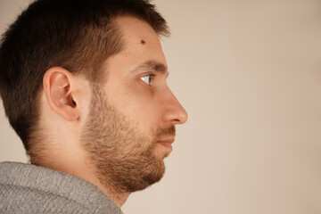 Obraz premium Handsome male. Side view. Neutral background. Man in casual clothes. Young man standing in front of camera. Guy looking at side. Perfect cheek.