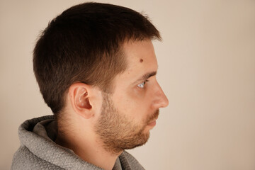 Fototapeta premium Neutral background. A guy in casual clothes. Young man standing in front of camera. Male looking at side. Good hair condition. Handsome man. Side view.