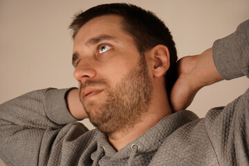 Obraz premium Crossed hands over head. Young male standing in front of camera. Man looking at camera. Man in casual clothes with neutral background. A handsome guy.