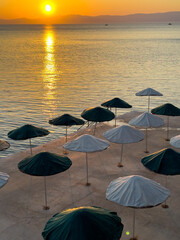Sunrise over calm waters with beach umbrellas arranged neatly along the shore at a serene coastal location