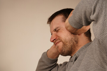 Fototapeta premium Portrait of young guy closing his ears by hands and keeping his eyes closed while isolated on grey. Photo of desperate annoyed bearded man keeps hands on head and closes eyes. Man in depression.
