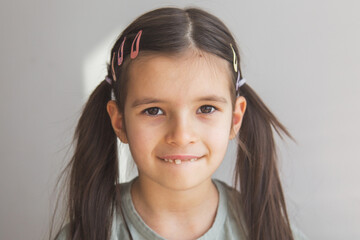 close-up portrait of a 6 year old brunette girl with two ponytails, looking at camera, showing one front tooth that has fallen out