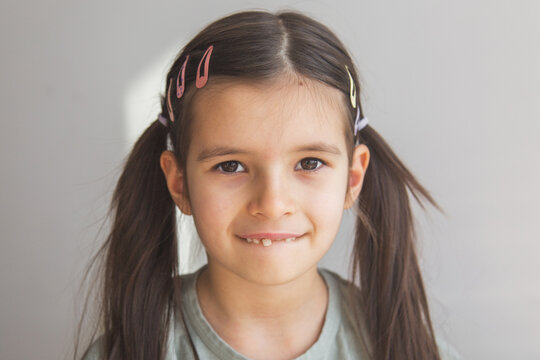 close-up portrait of a 6 year old brunette girl with two ponytails, looking at camera, showing one front tooth that has fallen out