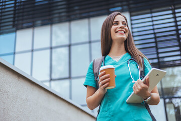 Young Nurse Smiling Outdoors with Coffee and Tablet