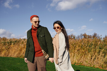 A loving couple strolls hand in hand through a picturesque autumn landscape, radiating warmth.