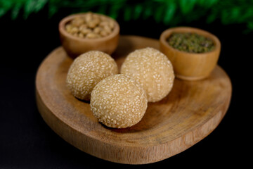 Onde-onde, a traditional snack from Indonesia, filled with green beans with chewy sticky rice skin and sprinkled with sesame seeds, placed on a wooden tray that looks very natural