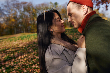 A couple shares a tender moment, wrapped in warm autumn attire, surrounded by colorful leaves.