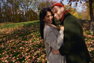 A couple enjoys each others warmth in cozy autumn outfits surrounded by colorful leaves.