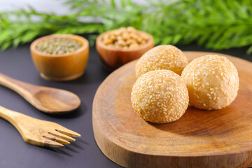 Onde-onde, a traditional snack from Indonesia, filled with green beans with chewy sticky rice skin and sprinkled with sesame seeds, placed on a wooden tray that looks very natural