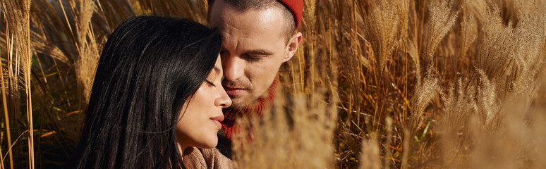 A loving couple shares a tender moment surrounded by tall, swaying grasses in autumn.