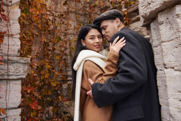 A charming couple dressed in autumn layers enjoys a tender moment amidst colorful leaves.