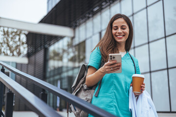 Smiling Nurse Checking Smartphone While Holding Coffee Outside Hospital