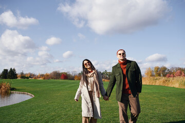 A loving couple enjoys a warm walk together, surrounded by vibrant autumn foliage and blue skies.