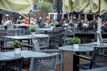 A charming café in Leiden, Netherlands, with outdoor seating by a canal. Features white tables with potted plants, wicker chairs