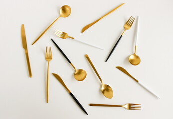 Modern cutlery set pattern gold black white colors on light beige background top view . Elegant table setting.