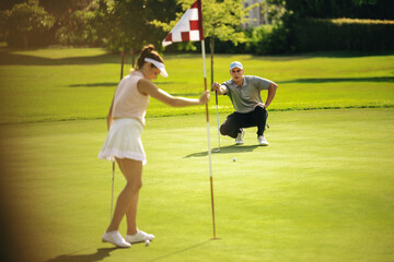 Golfers on putting green, with flagstick visible in a sunny golf course.