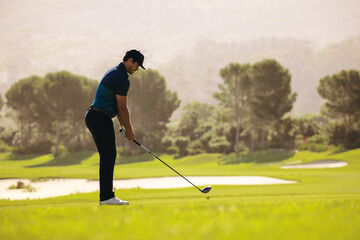 Professional golfer prepares for a powerful tee shot near a sand bunker, focusing intently on the challenging golf course ahead