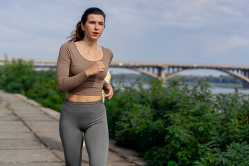 on the street on the river embankment in the city center on  concrete path a sporty girl in a gray sports suit healthy lifestyle morning jogging imperfect figure