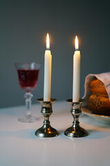 vertical photo Shabbat or Sabbath kiddush ceremony composition with a traditional sweet fresh loaf of challah bread, glass of red kosher wine and candles on a vintage wood table with copy space