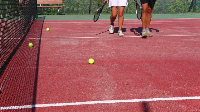 Close-up of an elderly couple's legs as they walk on the tennis court, holding their racquets