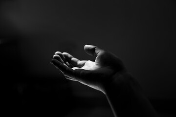Main tendue vers la lumière, clair obscur sur fond noir.